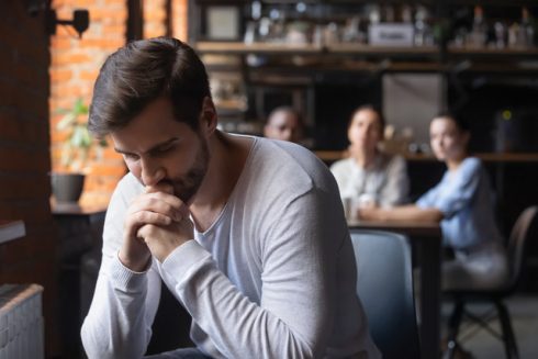 Sad Guy Sitting Alone Separately From Other Mates In Cafe