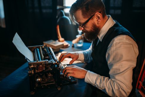 Bearded Journalist In Glasses Typing On Typewriter